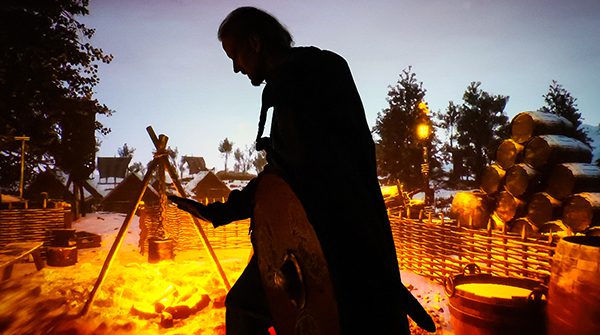 A silhouette of a person in front of a large LED screen displaying a fire and cooking pots.