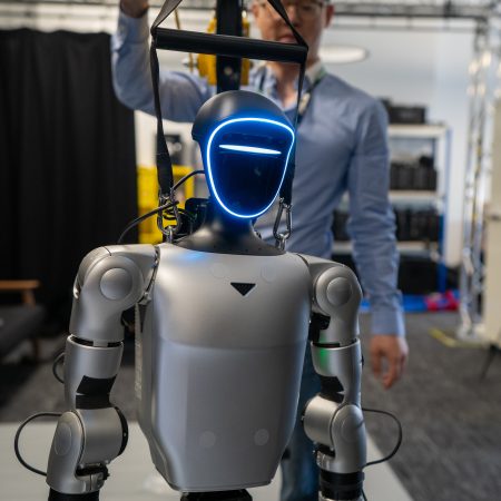Steven Dai stands behind a humanoid robot suspended on a pulley system in the XR Stories immersive R&D facility