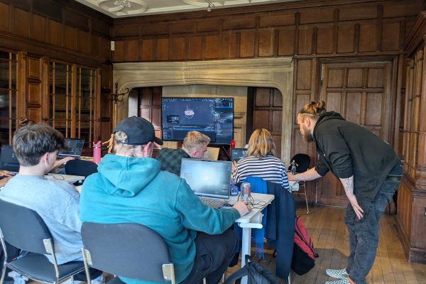 An Extending XR creative technology skills development workshop. People sit working on tablet devices and laptops while a trainer leans over to support learning.