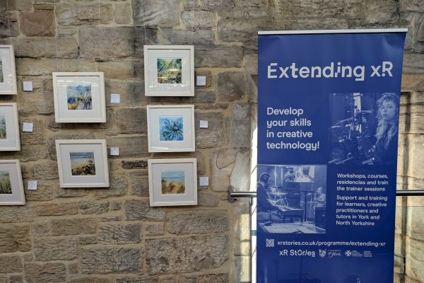 An Extending XR roller banner stands next to eight small paintings mounted on a brick wall at Woodend Gallery and Studios in Scarborough